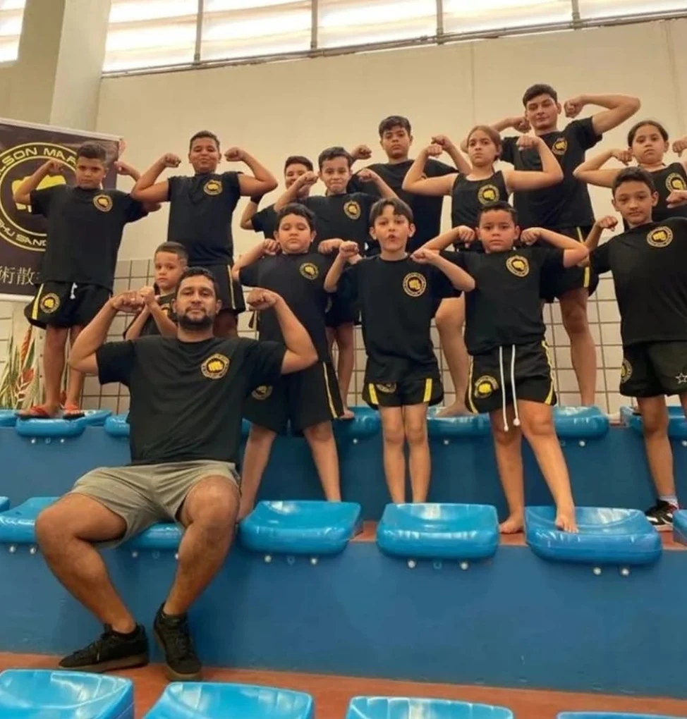 Grupo de crianças e instrutor do CT Garagem em pose de força durante aula de artes marciais em Osasco